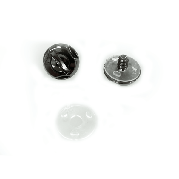 Three fastener components are placed against a white background: a black two-holed button, a clear round plastic piece with holes, and a shiny metallic screw component with a flat base and a threaded shaft.
