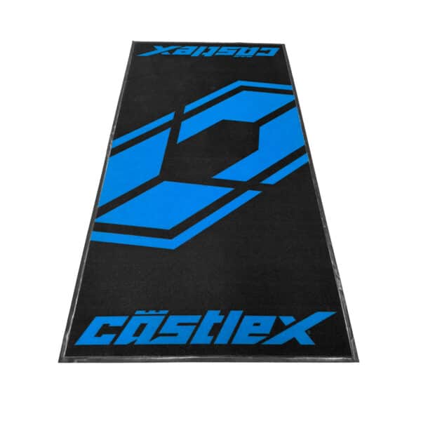 The Castle X Shop Mat is a rectangular black mat with a large blue geometric design in the center and "Cästlex" in blue text at one end.